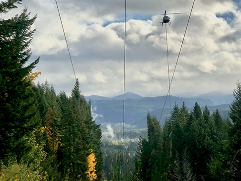 A helicopter with a saw attachment trims tree branches along EWEB's Carmen-Smith transmission line corridor.