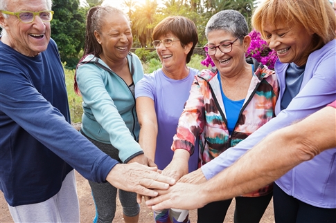 A group of older adults in a park put their hands together as a team.