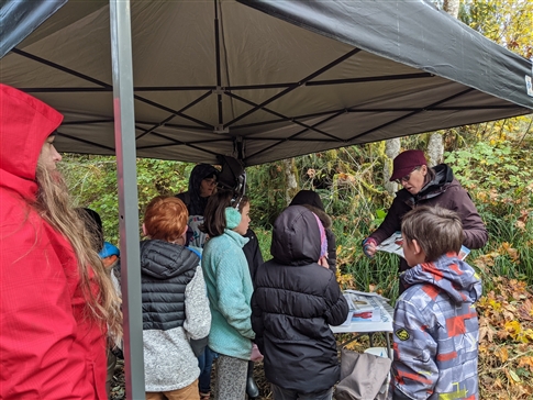 students gather under an awning with a teacher