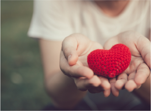 Hands holding out a tiny, knitted red heart 