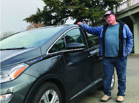 Man standing next to dark grey Chevy Bolt