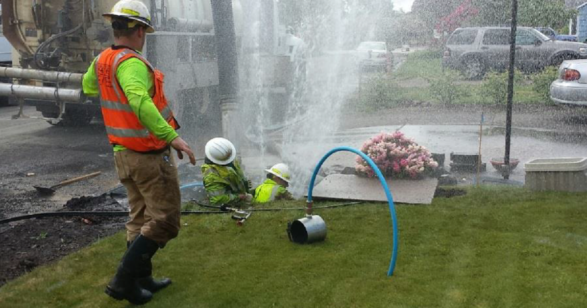 Picture workers fixing a broken water pipe as water sprays high into the air