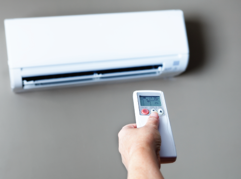 Hand holding a remote for adjusting the temperature of air conditioner