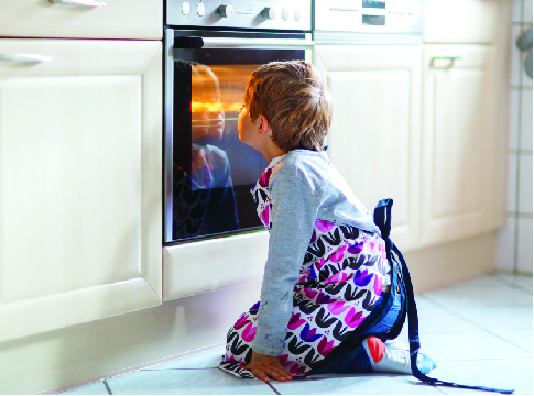 A young child starting through the oven door at something delicious cooking