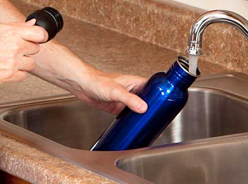 Person filling a blue water bottle from the kitchen sink.