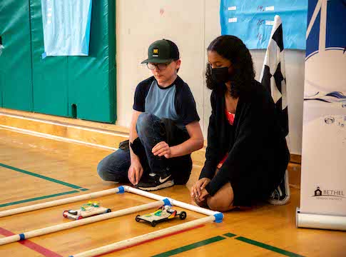 Students watching as student-built model solar electric cars take off from the starting line.