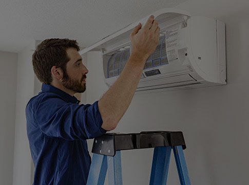 Man on a ladder looking at a ductless heat pump head unit.