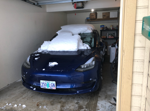 Blue Tesla Model 3 parked in garage with snow on the hood