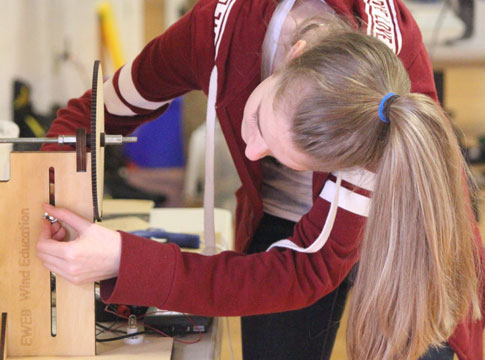 Middle school girl with pony tail adjusting the base of for her model wind turbine.