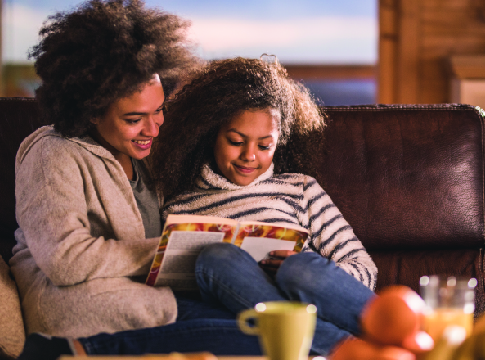 Mom and young daughter cozy on the couch reading a book together