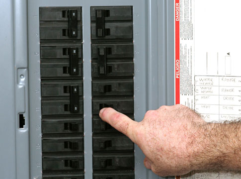 A man's hand flipping a breaker in a circuit panel.