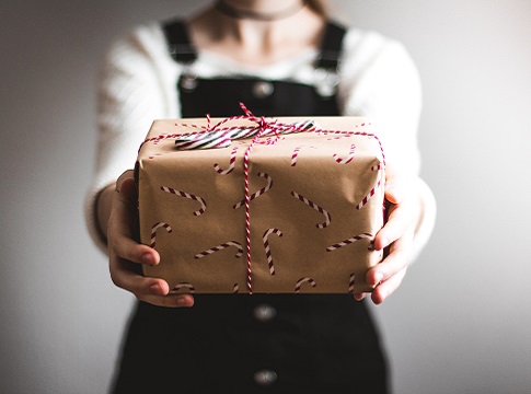 A woman holding out a brown paper-wrapped package with red and white ribbons