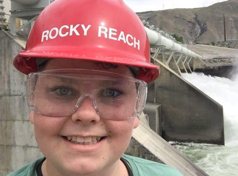 Male student in a hardhat standing in front of a dam