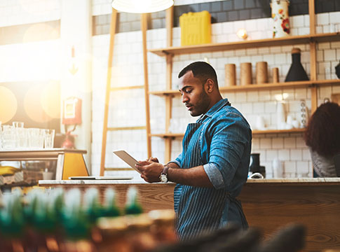 Man with apron in cafe looking at tablet