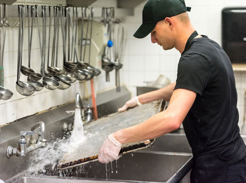 Man washing large tray in a restaurant kitchen.