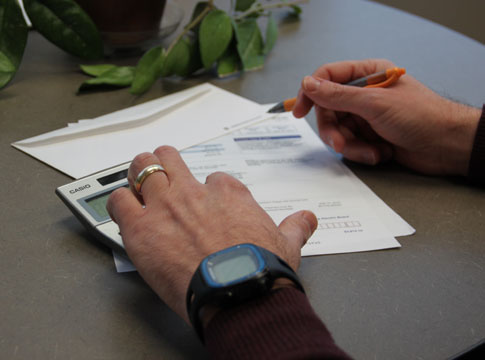 Hands holding a pen and calculator, bills on the desk