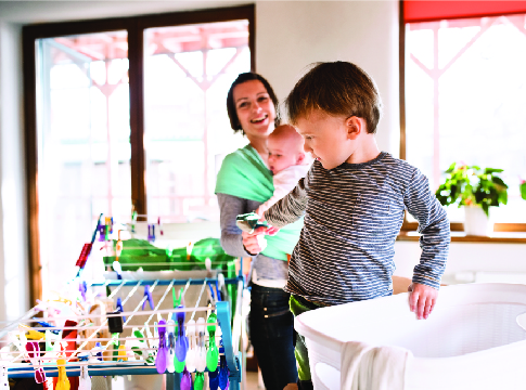 Mom holding baby and young son hanging clothes on a drying rack