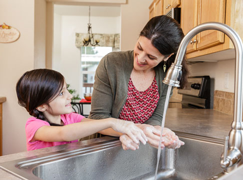mom and daughter washing hands at kitchen sink