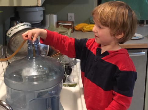 Young boy filling water container at the kitchen sink