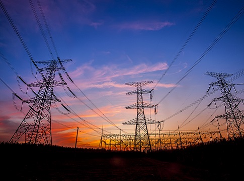 Electric transmission towers silhouetted against a sunset.