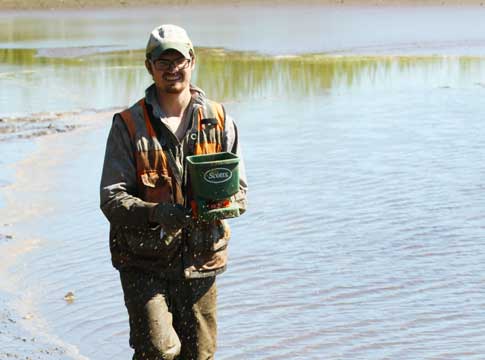 Man spreading seed at Walterville Pond