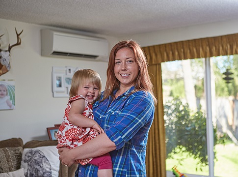 mother holding her daughter with a ductless heat pump in the background
