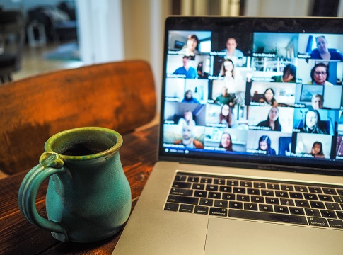 Laptop computer with a virtual meeting displayed and a cup of coffee on the table