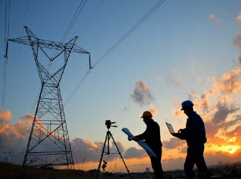 2 utility workers surveying a transmission tower with sunset in the background