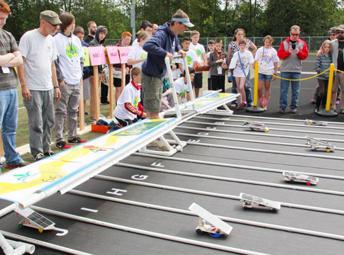 Students and teachers watching as student-built model cars take off from the starting line.