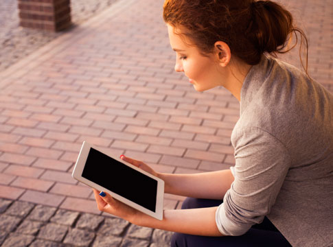 Woman sitting on a bench outside with a tablet.
