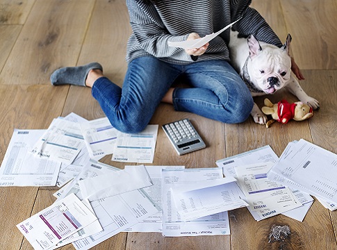 Woman sitting on the floor with her dog, bills spread out around her