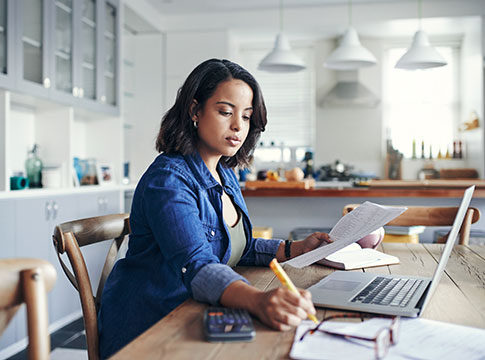 Woman at kitchen table with laptop paying bills