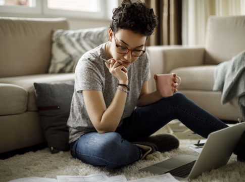 Young woman working from home, sitting on floor with laptop and cup of coffee