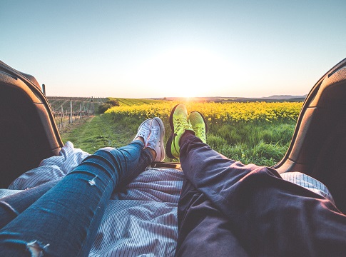 Couple's legs facing out the back of a car with a sunset view