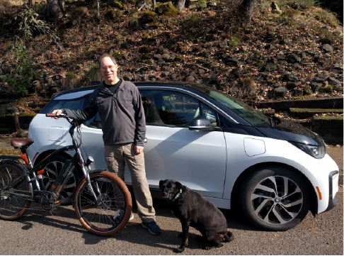 EWEB customer and his dog standing next to white BMW i3 electric car while holding an electric bike