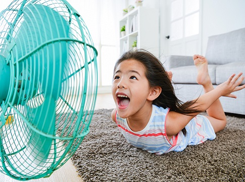 Young playful girl on the floor smiling at a colorful electric fan