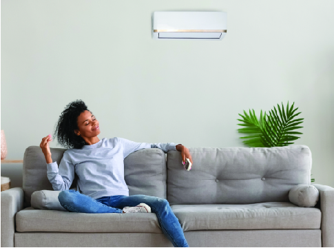 A young woman relaxing on a sofa with a ductless heat pump mounted on the wall