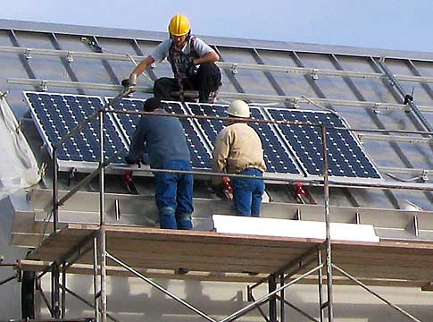 Workers installing photovoltaic solar panels on roof of building.