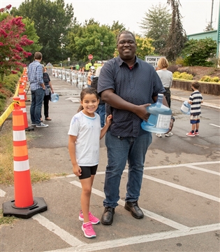 Father and daughter hold filled water jug at EWEB's emergency water station near Sheldon Community Center in Eugene.
