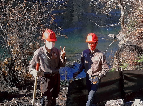 Two Northwest Youth Corps crew members in orange hardhats posting by McKenzie River