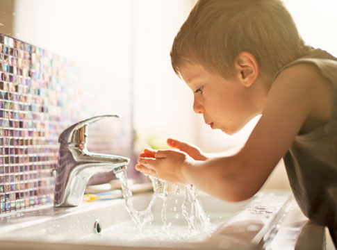 Little boy drinking at a sink with cupped hands